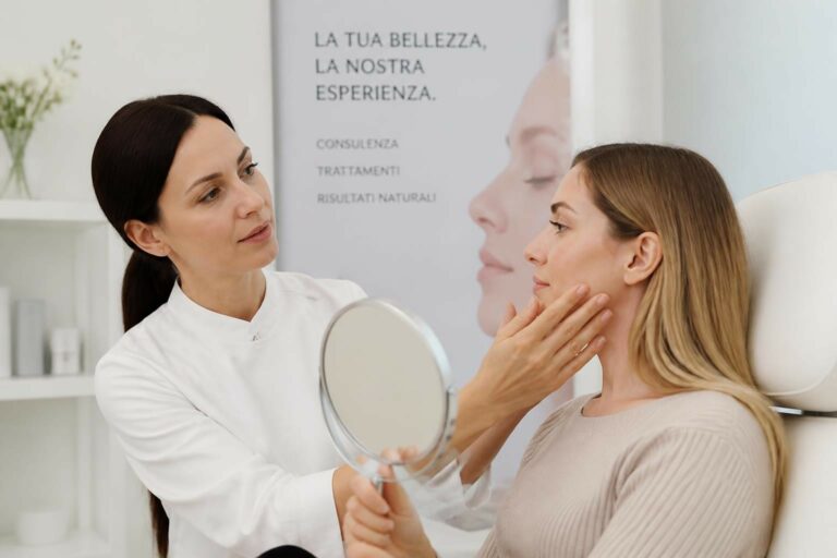 A clinician in white examines a woman's face, holding a round mirror during a skincare consultation.